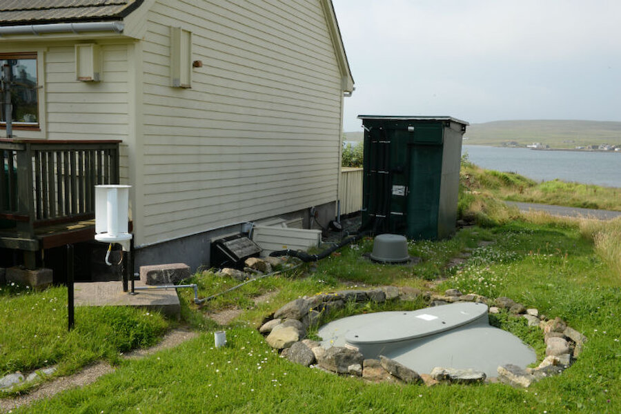 The small, white vertical-axis wind turbine on the left feeds energy into the large green hot water store, which is also fed by an air-to-water heat pump (Courtesy Alastair Hamilton)