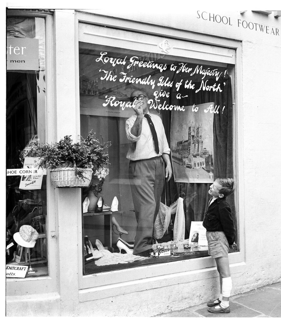 One of the photographs included in the exhibition: Attie Coutts signwriting in his shop window for the occasion of the Royal Visit in 1960 by Queen Elizabeth. (Courtesy Shetland Arts and Dennis Coutts)