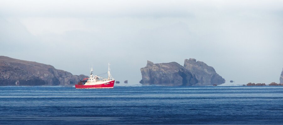A fishing boat passes Ramna Stacks to the north of Shetland Mainland. The industry is a major contributor to the Shetland economy.