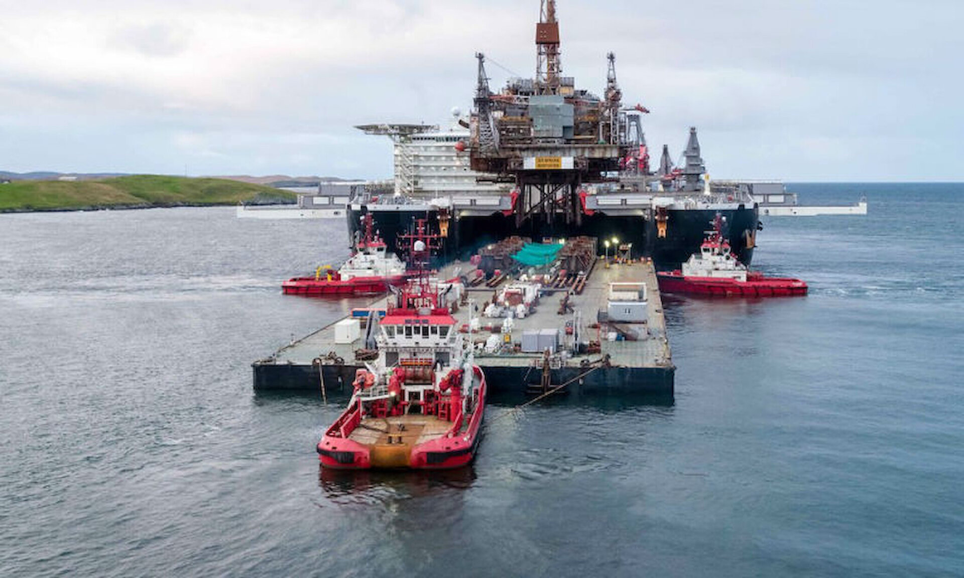 The barge, 'Iron Lady', is manoeuvered into position between the hulls of 'Pioneering Spirit', ready to receive the platform topsides in Lerwick Harbour.